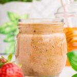 A mason jar of strawberry vinaigrette with a strawberry and basil on the side.