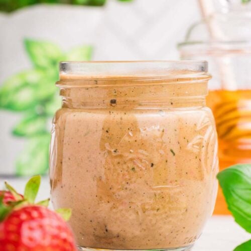 A mason jar of strawberry vinaigrette with a strawberry and basil on the side.