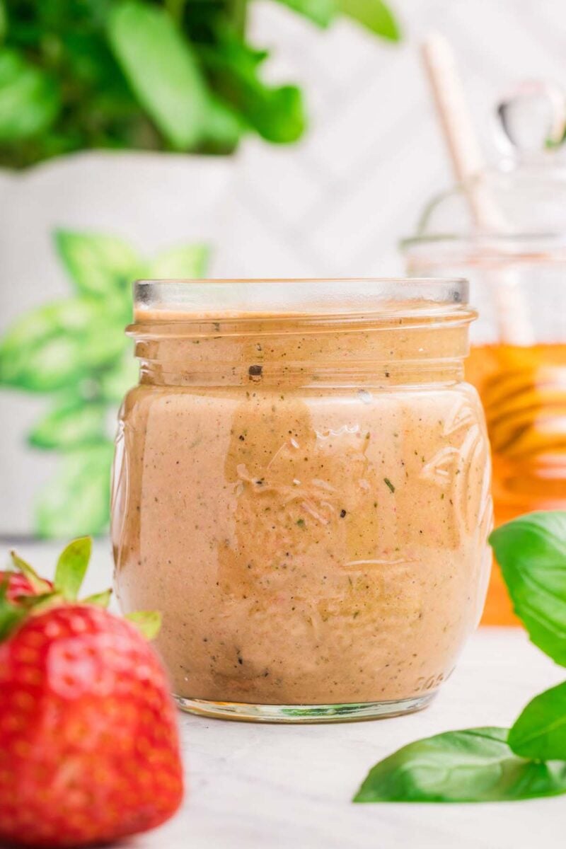 A mason jar of strawberry vinaigrette with a strawberry and basil on the side.