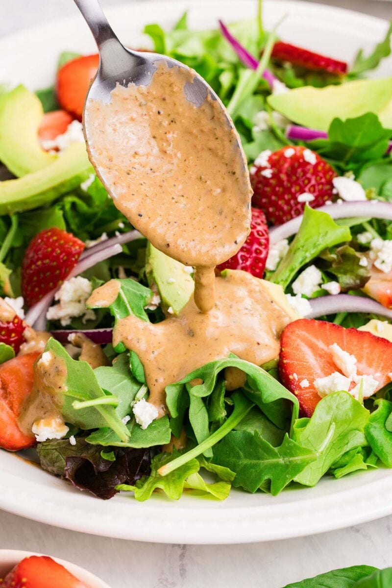 A spoon drizzling strawberry vinaigrette over a salad.