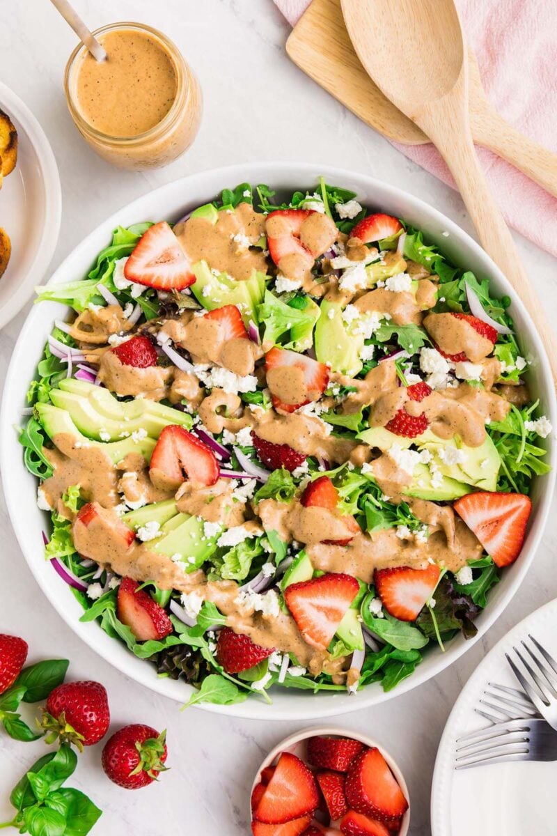 An overhead shot of a market salad topped with a strawberry vinaigrette with a jar of the vinaigrette on the side.