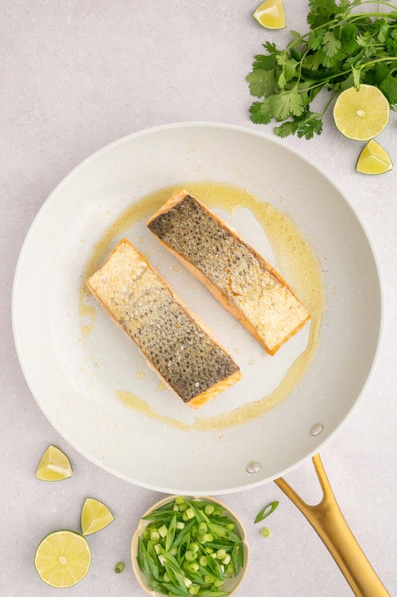 Salmon filets in a pan skin side up with fresh ingredients on the side.