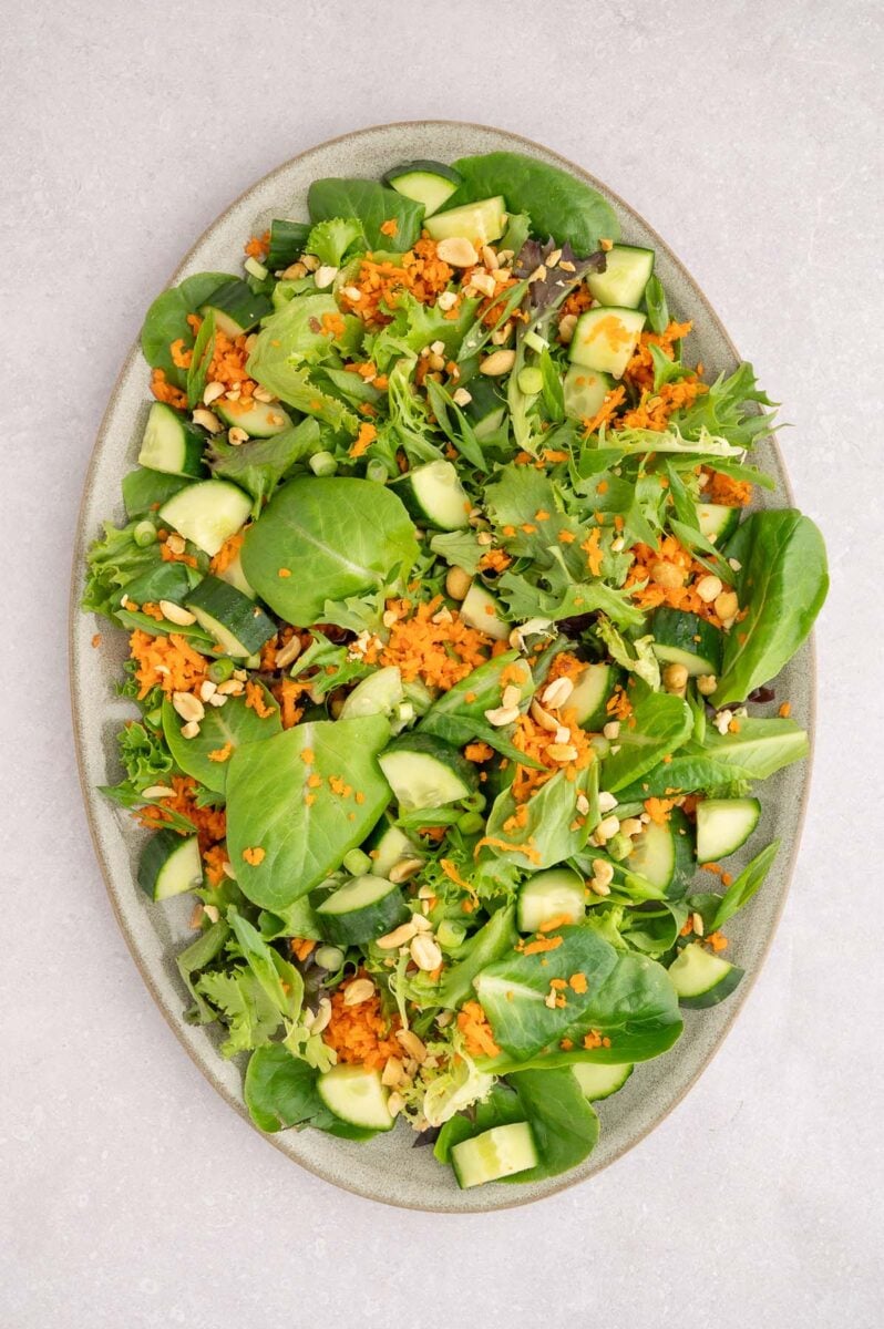 A salad with greens, cucumbers, carrots, and peanuts on a large platter.