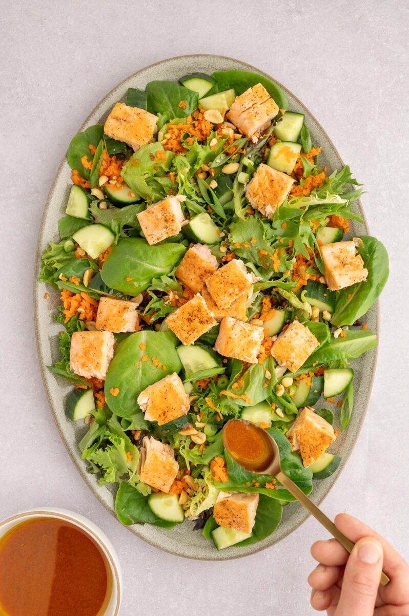 Sweet chili salmon salad on a large platter with dressing being drizzled on top.