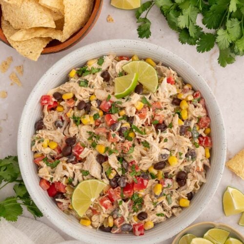 Taco Chicken Salad in a white bowl with bowls of tortilla chips and sliced limes and fresh cilantro on the side.
