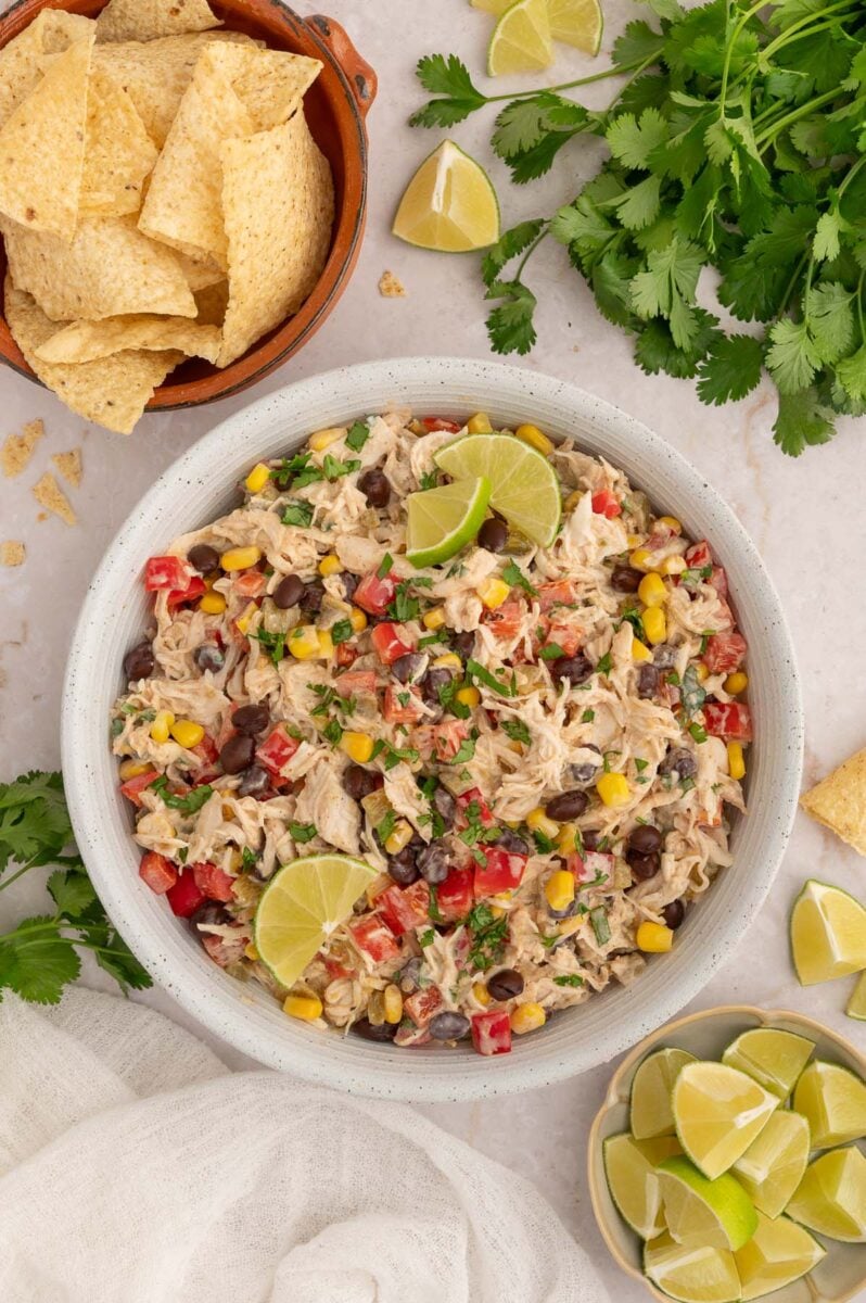 Taco Chicken Salad in a bowl with slices limes and tortilla chips in bowls on the side.