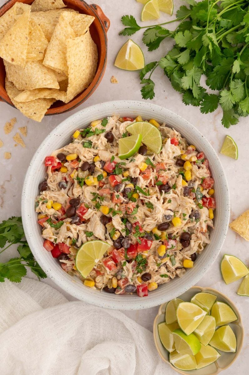 Taco Chicken Salad in a white bowl with bowls of tortilla chips and sliced limes and fresh cilantro on the side.