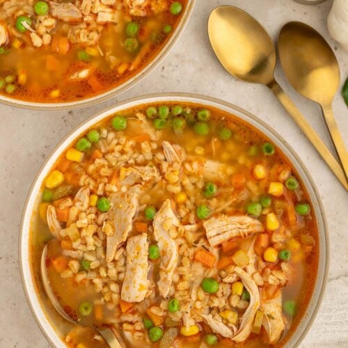 A bowl of Chicken Barley Soup with a spoon in it and another bowl on the side.