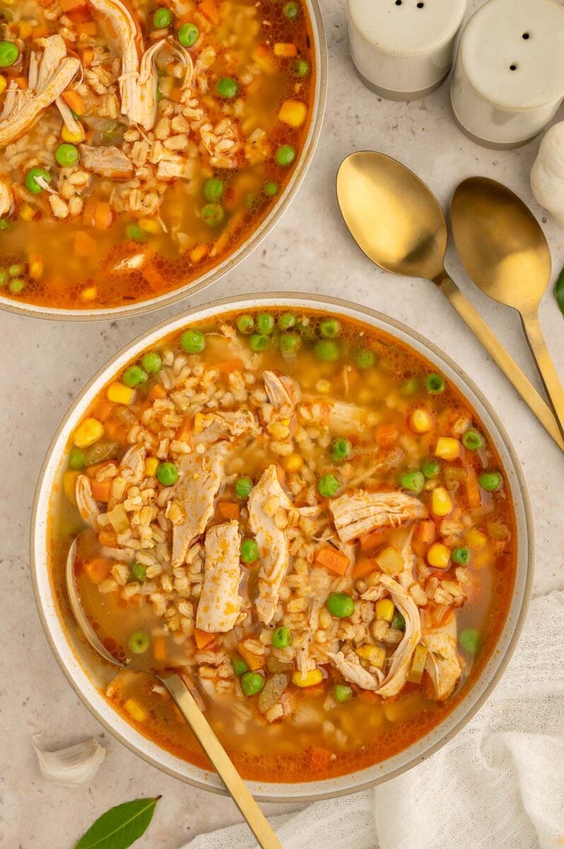 A bowl of Chicken Barley Soup with a spoon in it and another bowl on the side.