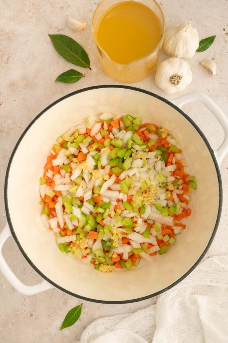 Chopped onion, celery, and carrots in a dutch oven cooking in oil for chicken barley soup. 