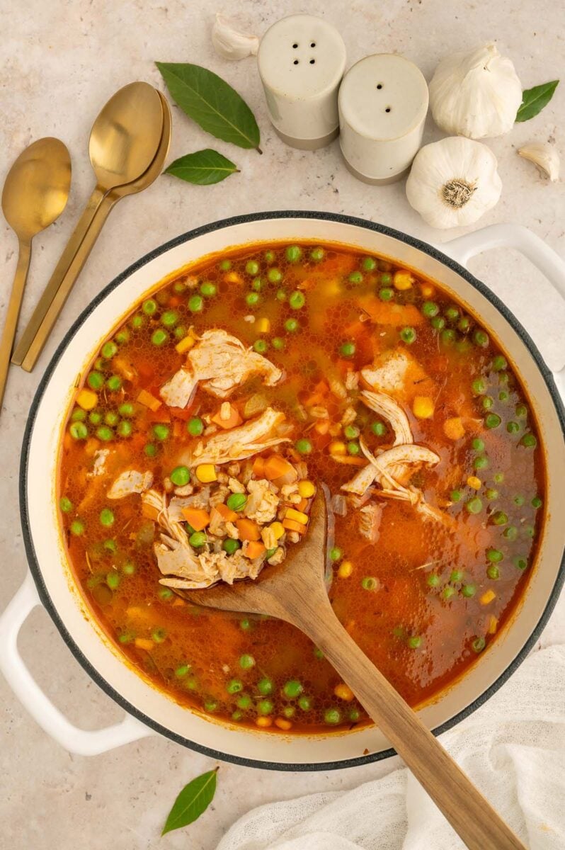 An overhead shot of a dutch oven of chicken and barley soup with a wooden spoon in it. 