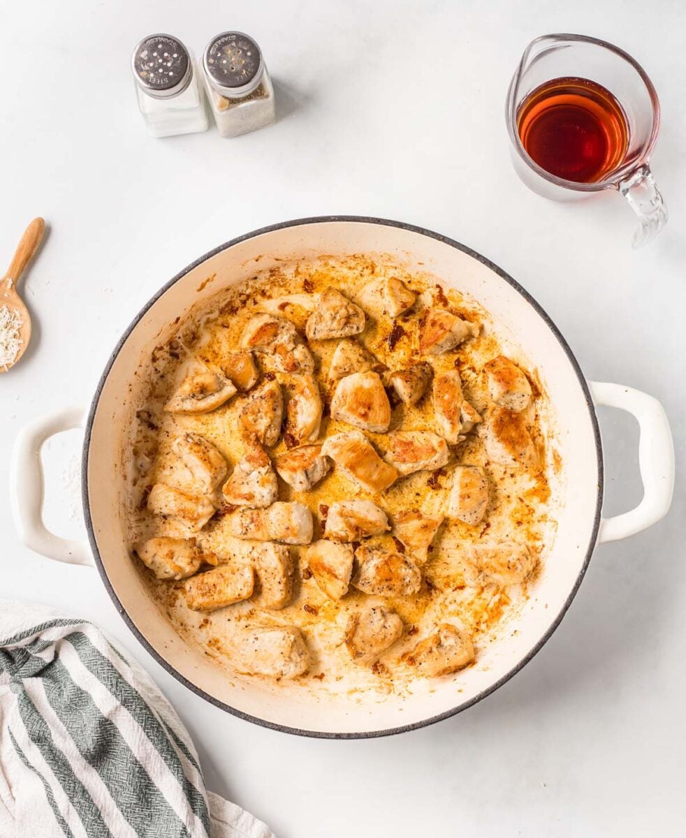 Chicken pieces cooking in a large dutch oven with marsala wine on the side.