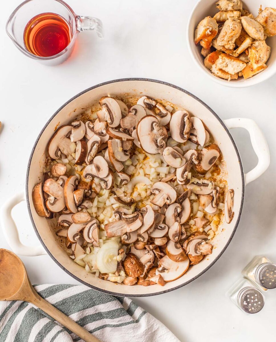 Mushrooms, garlic, and onion in a large pot with marsala wine and cooked chicken pieces on the side.