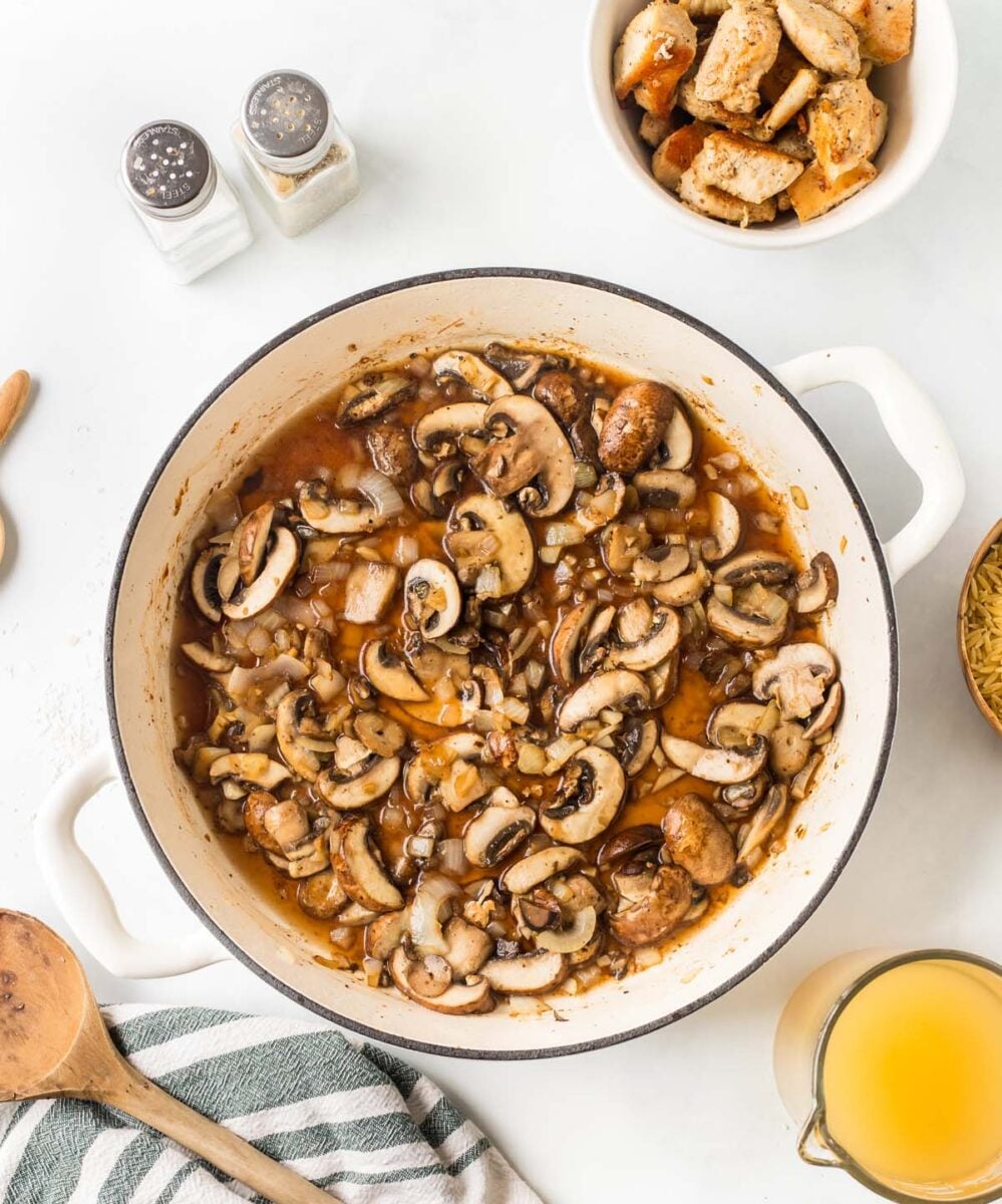Marsala wine added with mushrooms, garlic and onions in a dutch oven with a bowl of chicken on the side.