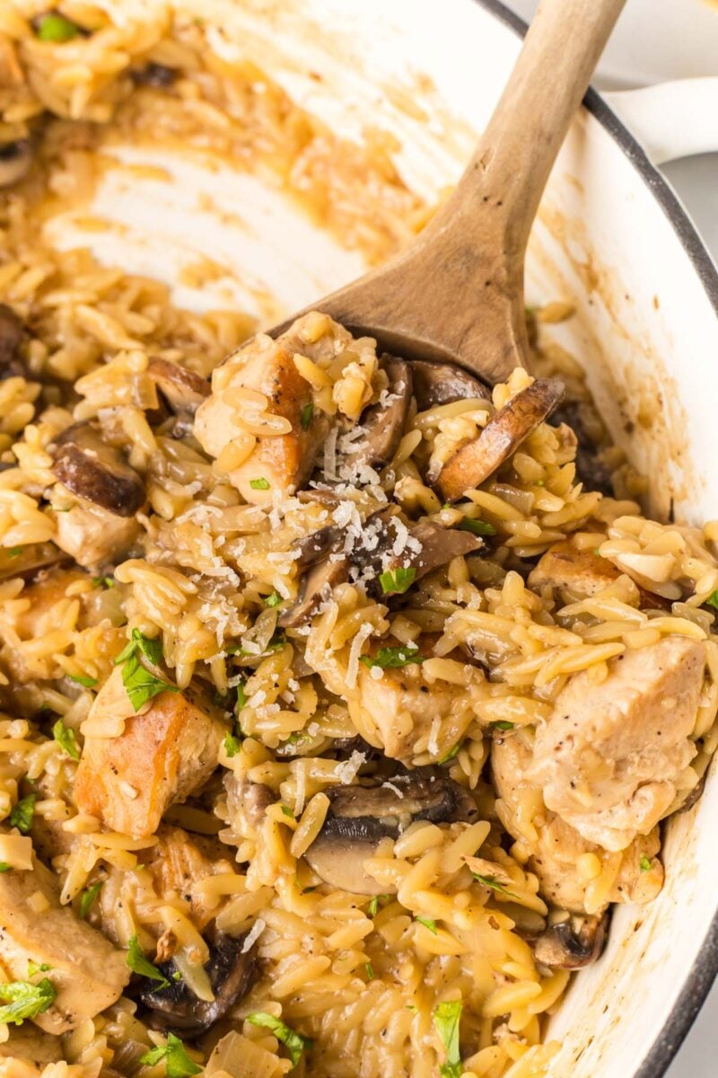 A wooden spoon taking a scoop into a pot of chicken marsala orzo.