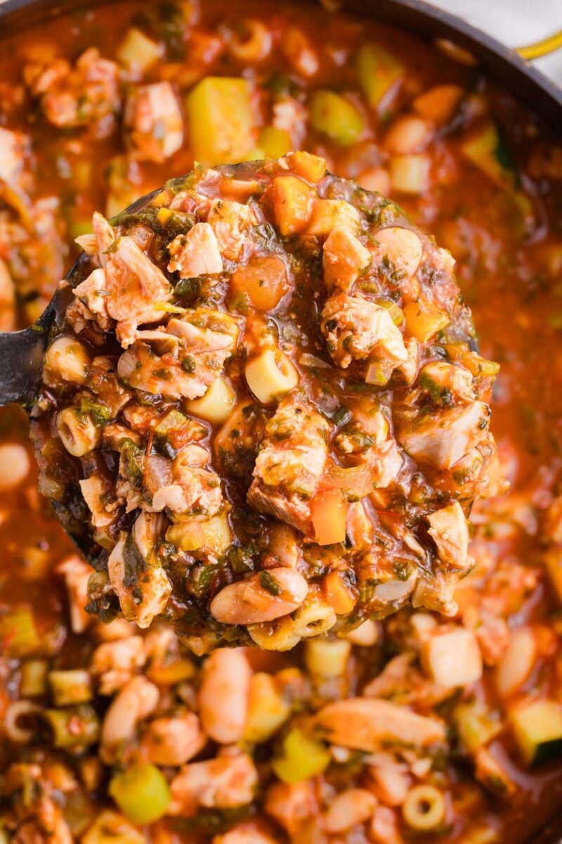 A ladle taking a scoop out of a pot of chicken minestrone soup in the background.