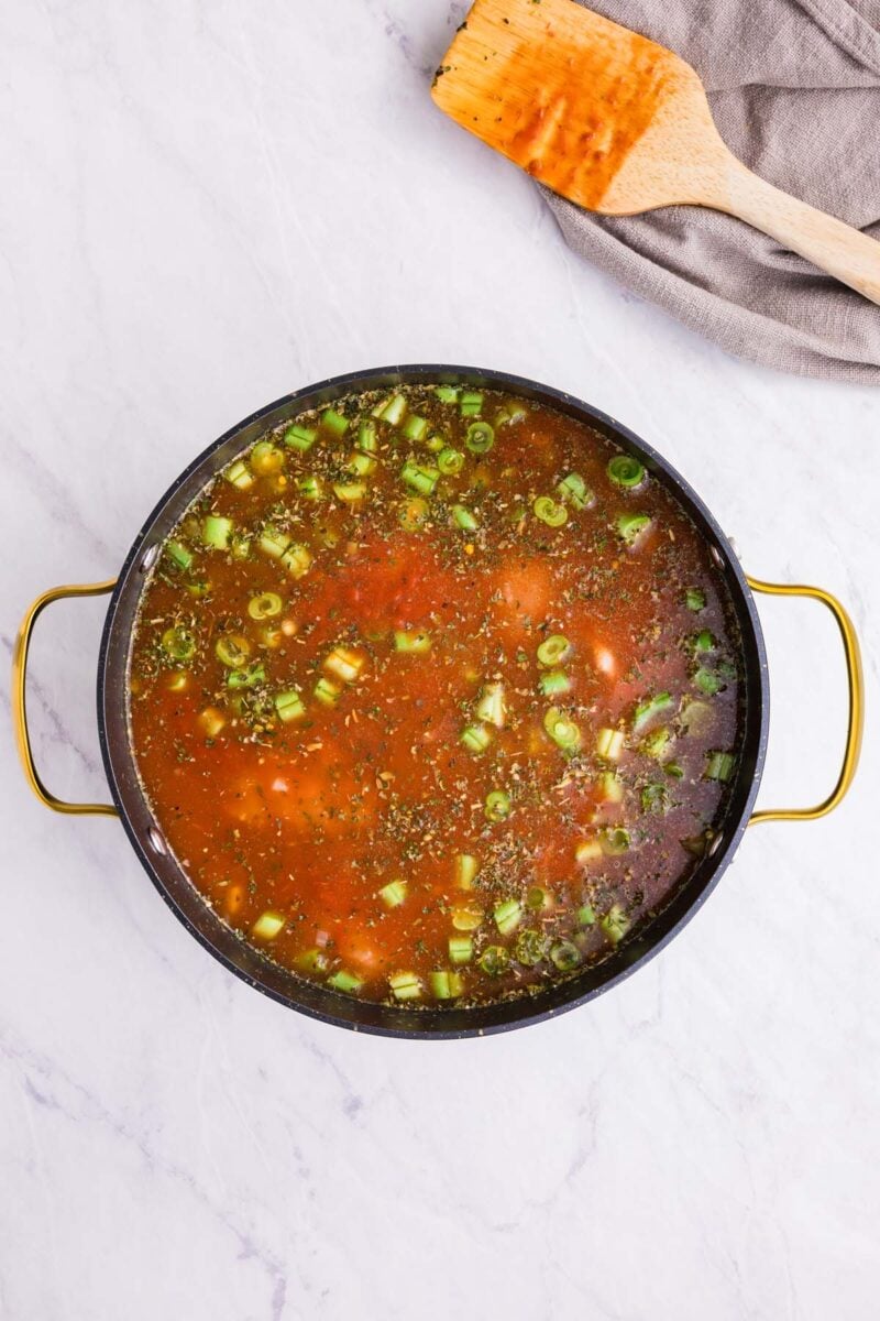 Chicken minestrone soup half cooked in a pot before chicken is shredded with a spoon on the side.