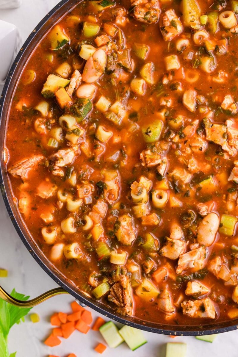 A large pot of chicken minestrone soup with chopped veggies on the side. 