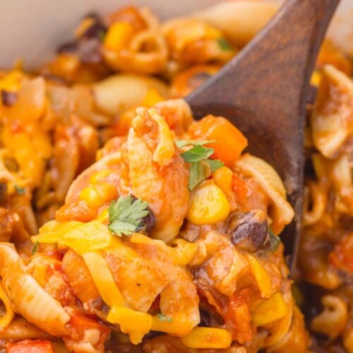 A wooden spoon taking a scoop out of a pot of Chicken Taco Pasta.