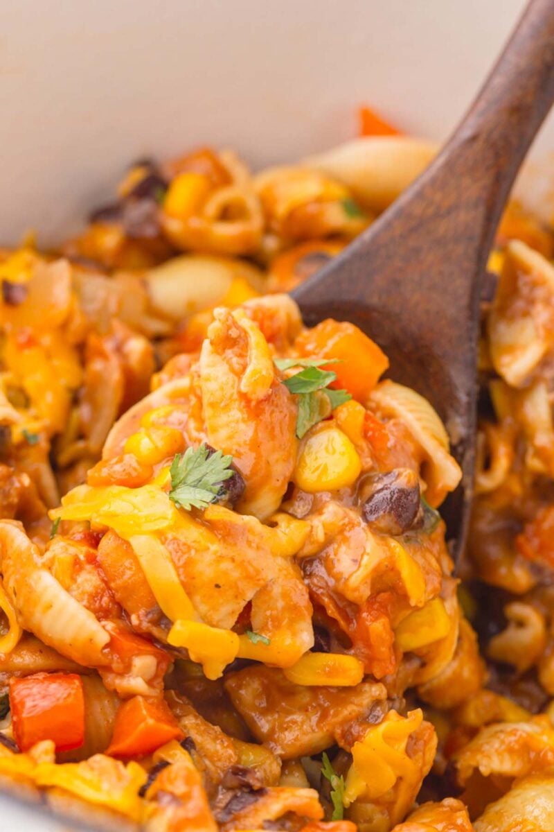 A wooden spoon taking a scoop out of a pot of Chicken Taco Pasta.