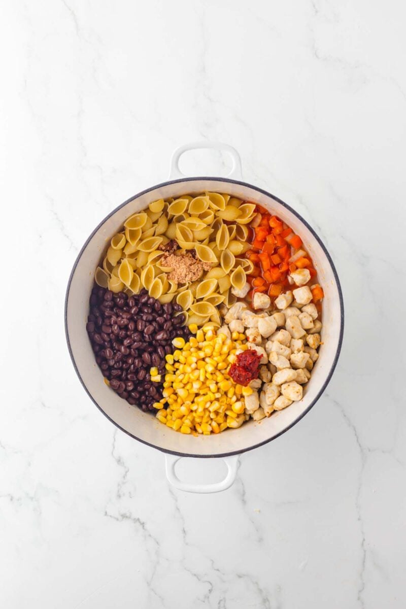 Ingredients for chicken taco pasta in a large pot before mixing together and cooking.