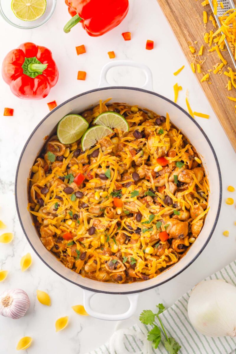Chicken Taco Pasta in a dutch oven garnished with lime slices and more ingredients on the side.