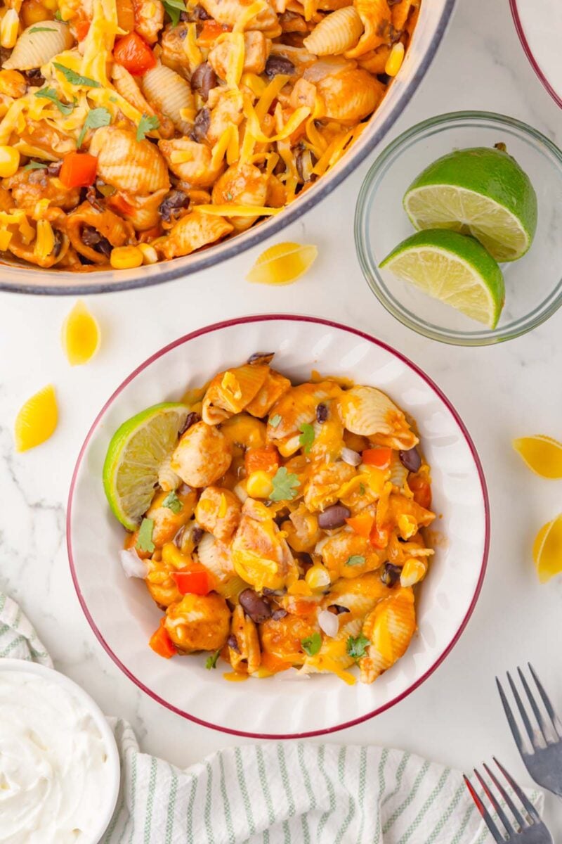 A plate of chicken taco pasta beside a pot of the pasta and lime slices on the side.