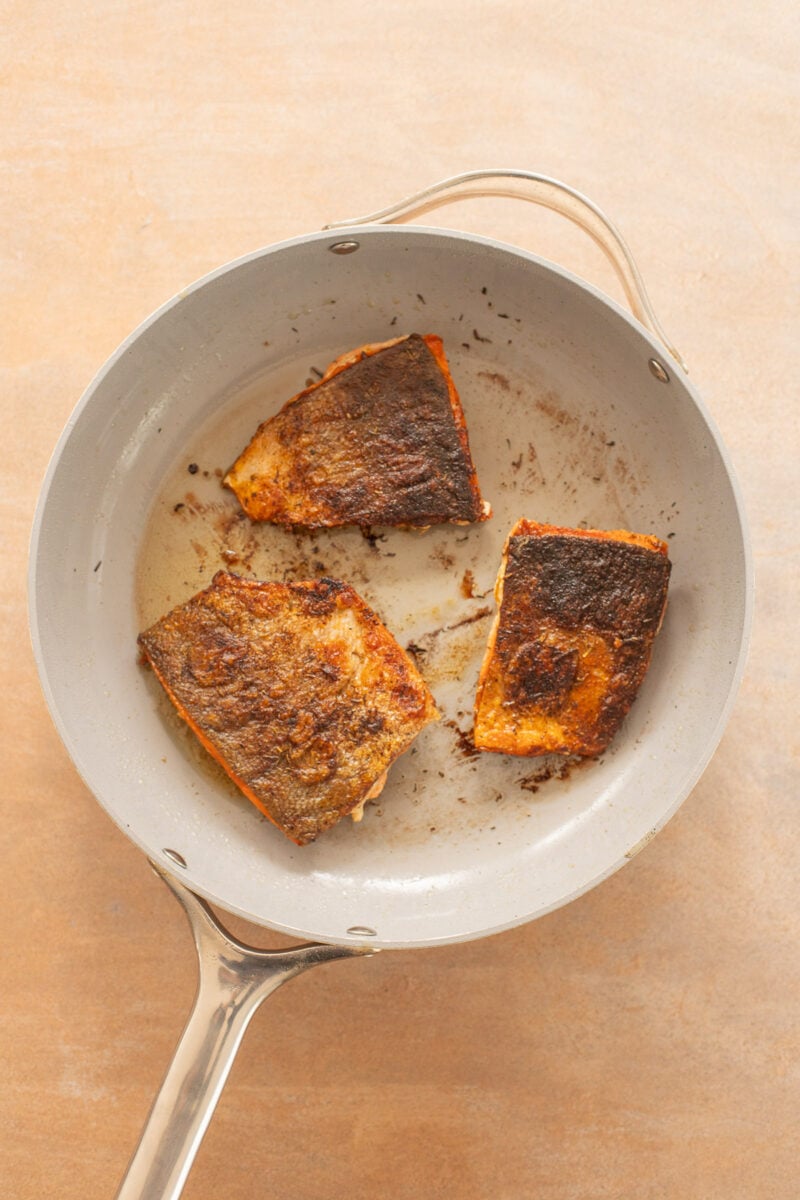 Three salmon filets cooking in a pan.
