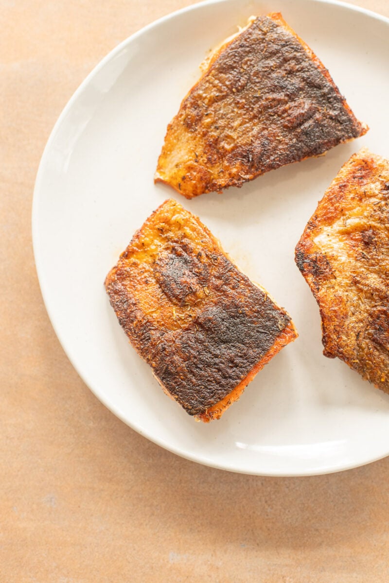 Three cooked salmon filets on a white plate.