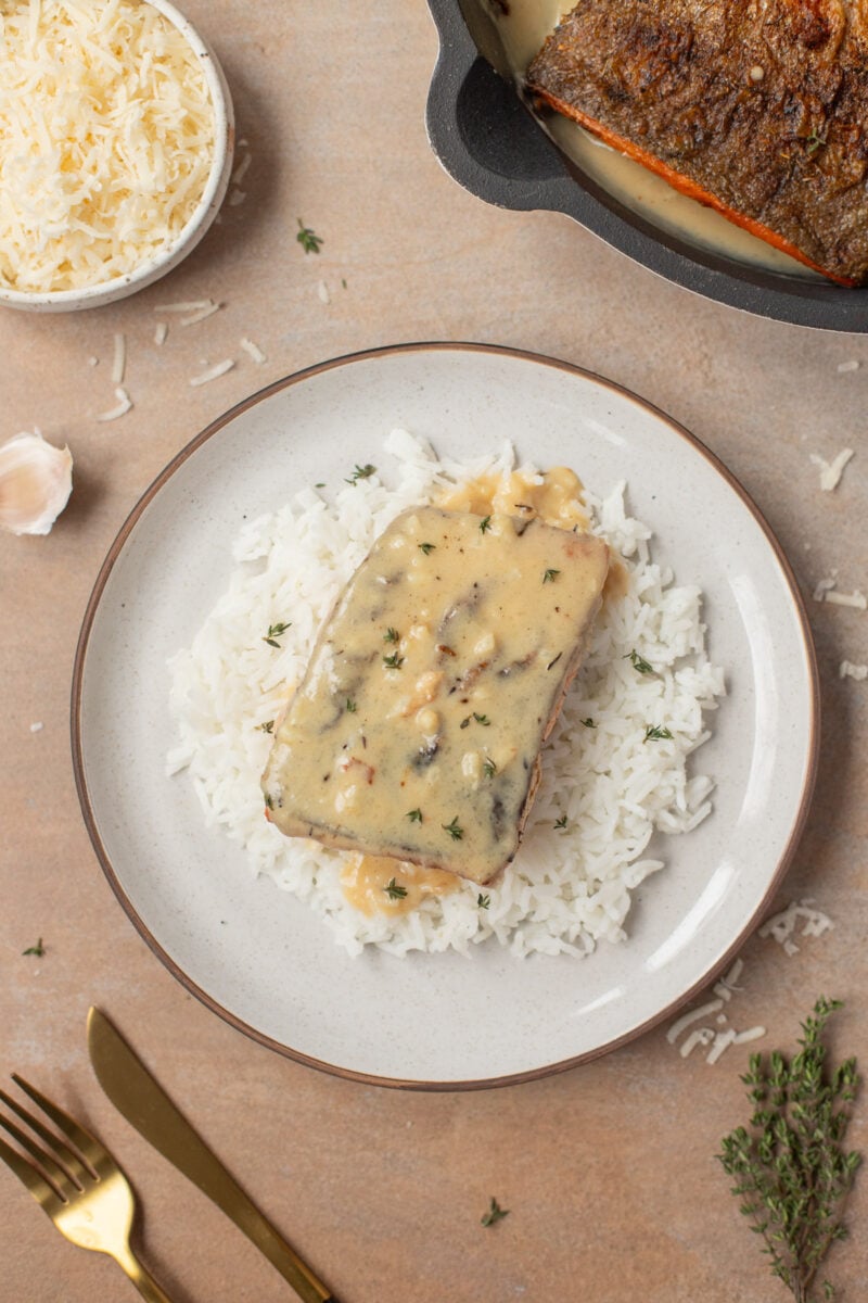 Creamy Garlic Salmon on a bed of white rice on a plate with a pan on the side.