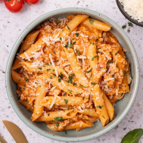 Ground Turkey Pasta in a bowl with tomatoes, cheese and herbs on the side.