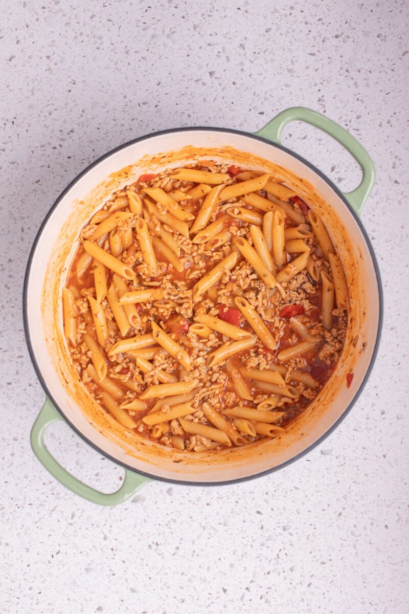 A large dutch oven of cheesy ground turkey pasta on a counter.