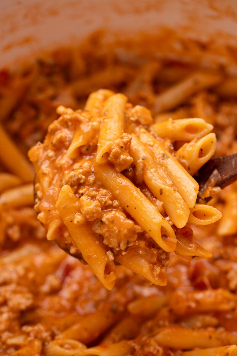 A ladle taking a scoop of cheesy turkey pasta out of a pot of the pasta.