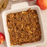 Healthy Apple Crisp in a white baking dish on a background with apples off to the side.