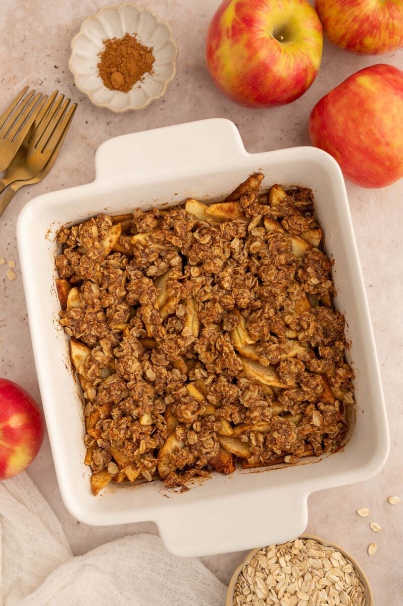 Healthy Apple Crisp in a white baking dish on a background with apples off to the side.