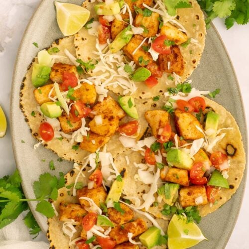 Four quick fish tacos on tortillas garnished with cabbage and lime slices.