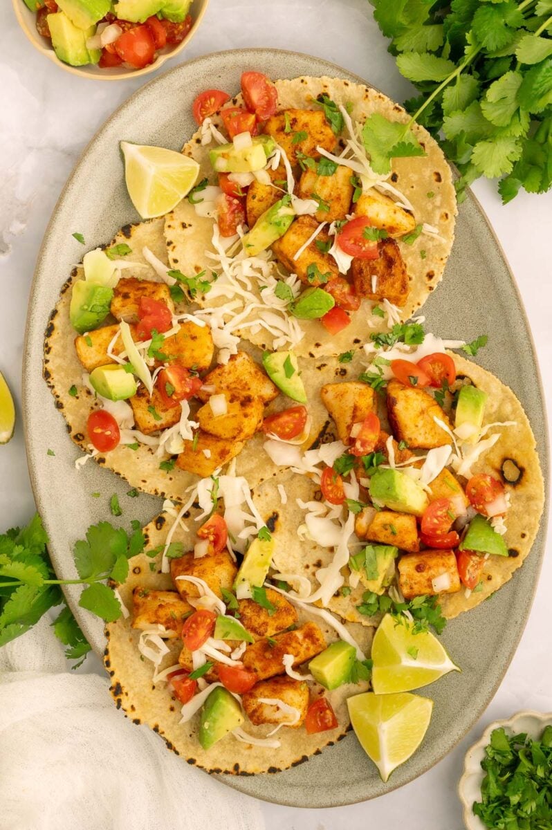 Four quick fish tacos on tortillas garnished with cabbage and lime slices.