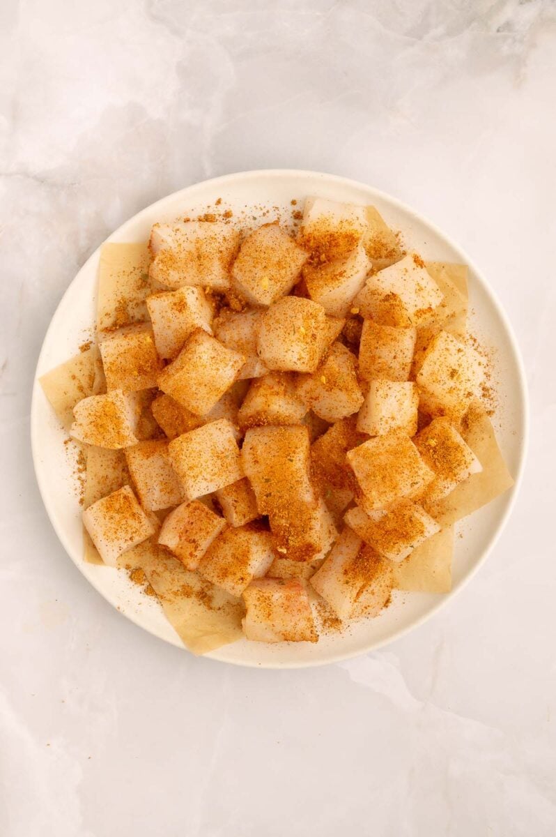 Seasoned uncooked halibut fish pieces on a plate.
