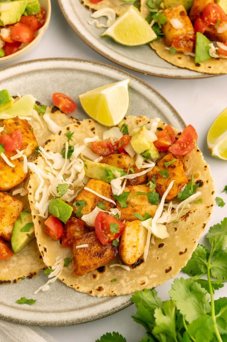 A Healthy fish taco on a tortilla topped with avocado tomato salad and cabbage.