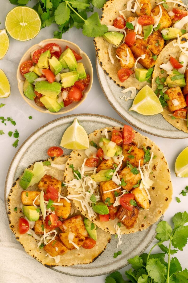 Two fish tacos on a plate with avocado tomato salsa on the side.