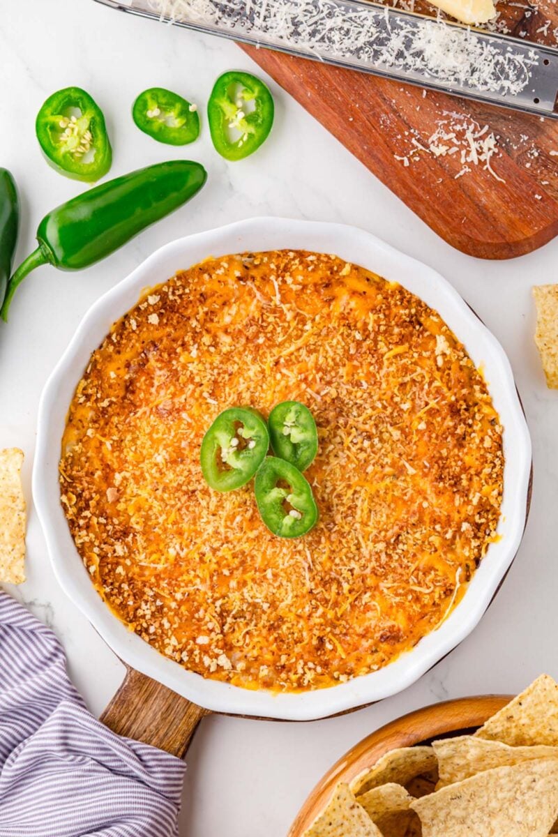 Healthy Jalapeno Popper Dip in a round white dish topped with jalapenos and surrounded by jalapenos and a wooden cutting board.