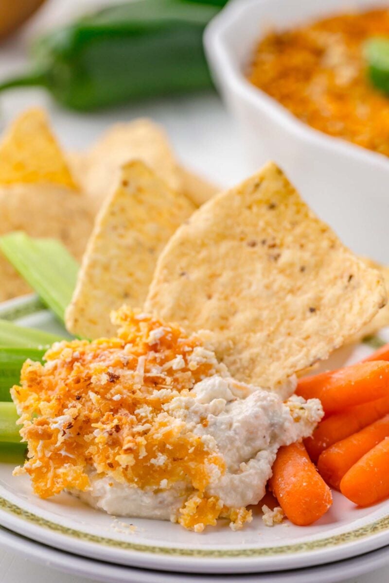 A plate with a serving of jalapeno popper dip with tortilla chips, carrots, and celery on the plate.