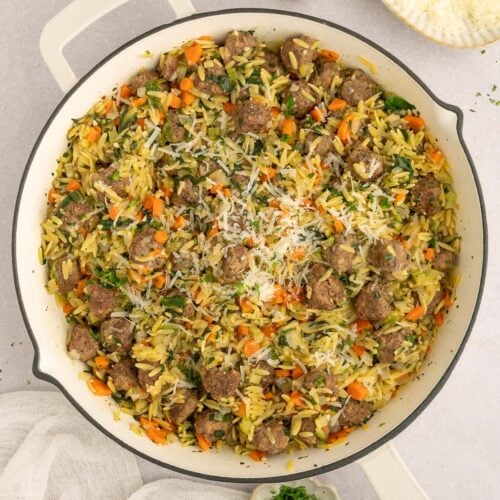 Italian wedding orzo in a skillet on a counter with fresh herbs and ingredients on the side.