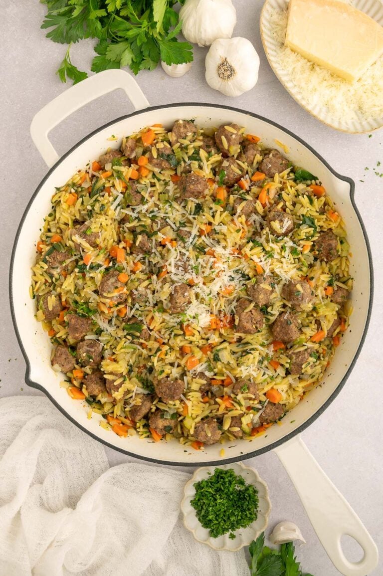 Italian wedding orzo in a skillet on a counter with fresh herbs and ingredients on the side.