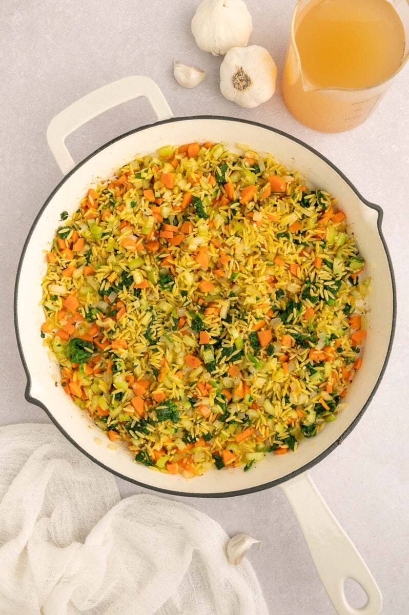 Italian wedding orzo cooking in a skillet before meatballs and cheese is added.