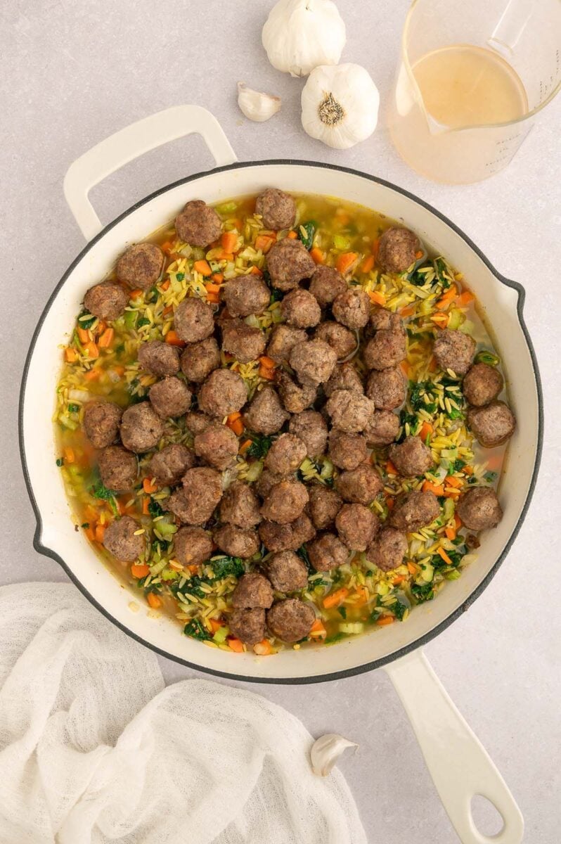 Meatballs and broth added to a skillet for italian wedding orzo. 