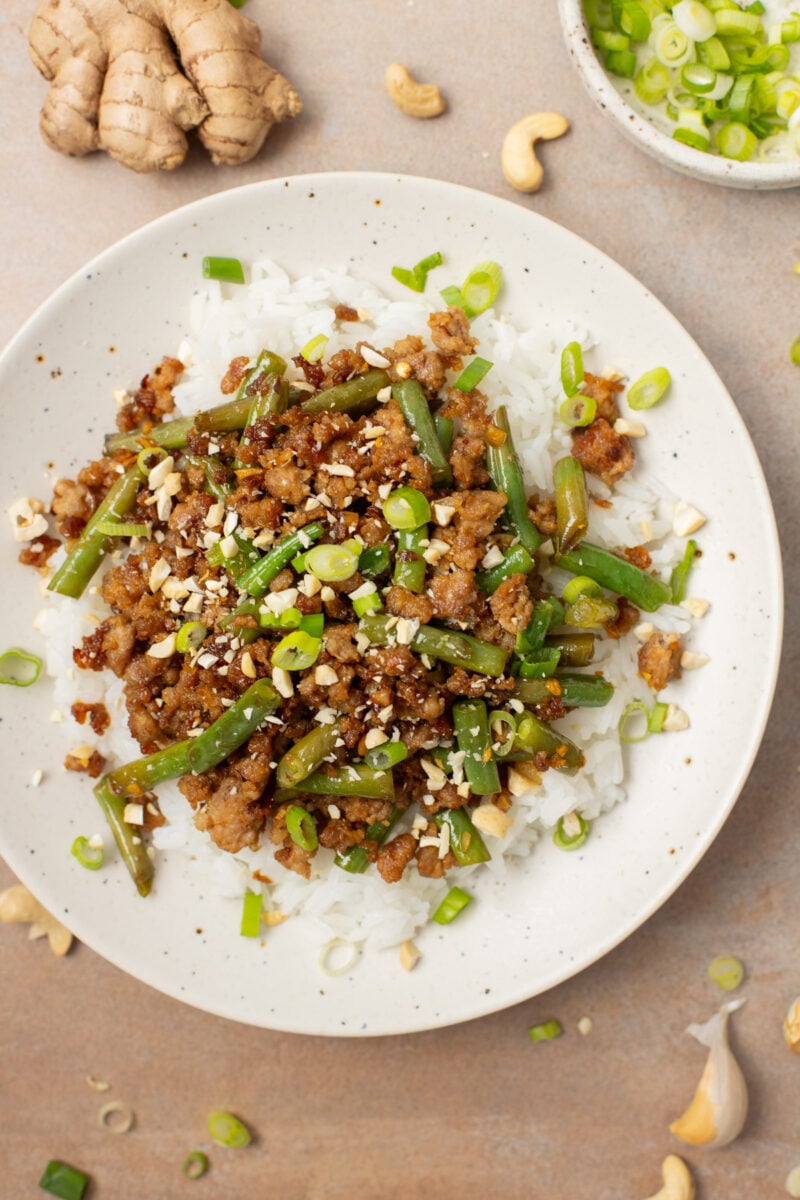 A plate of ground pork stir fry with green beans on a bed of white rice.