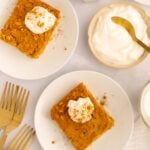 Pumpkin Baked Oatmeal servings on two white plates topped with whipped cream and cinnamon with a small bowl of whipped cream on the side.