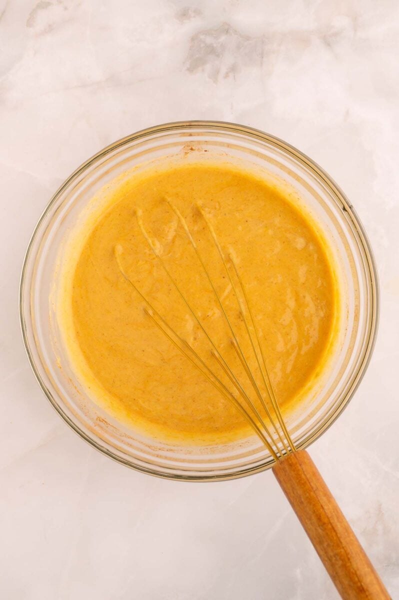 Liquid ingredients for pumpkin baked oatmeal in a clear glass bowl with a whisk in it.
