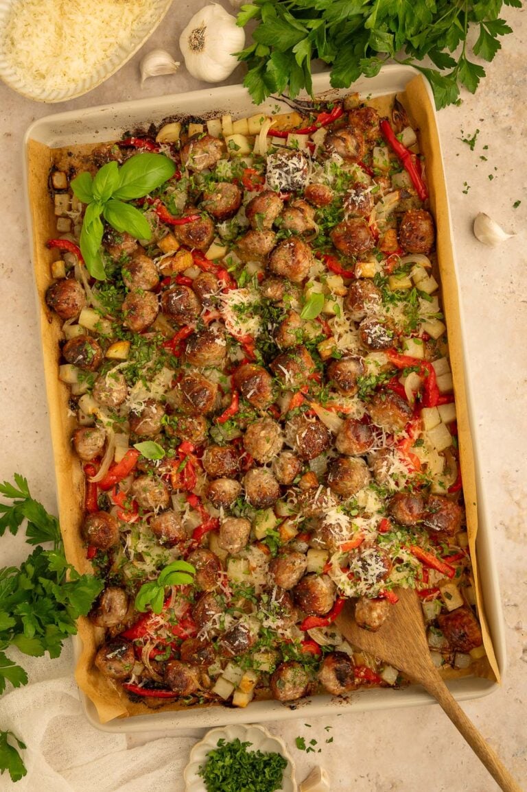 Sausage, peppers, potatoes, and onions on a sheet pan with a wooden spoon in it.